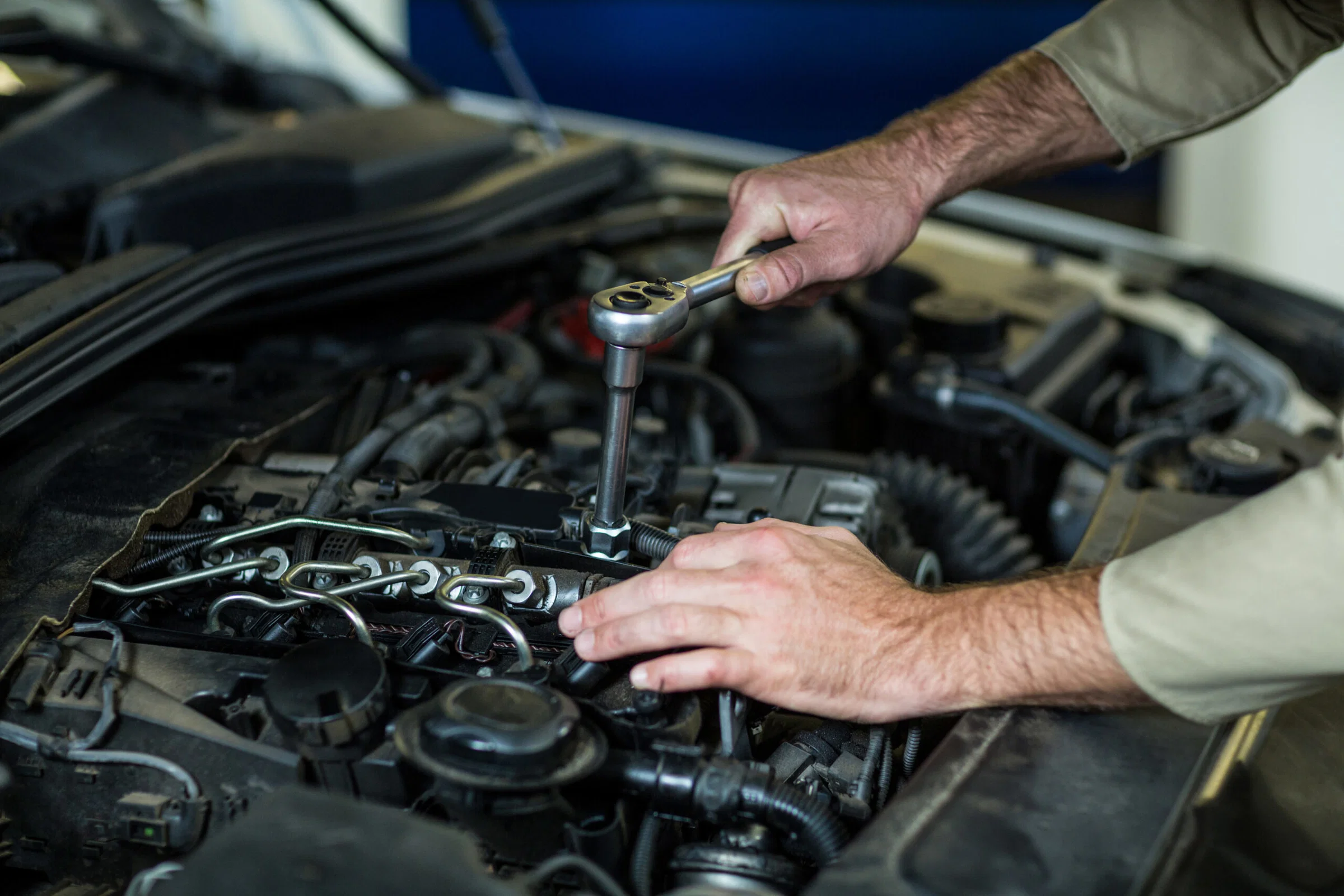 A person uses a ratchet wrench to tighten or loosen a bolt on a car engine in an auto repair workshop setting.