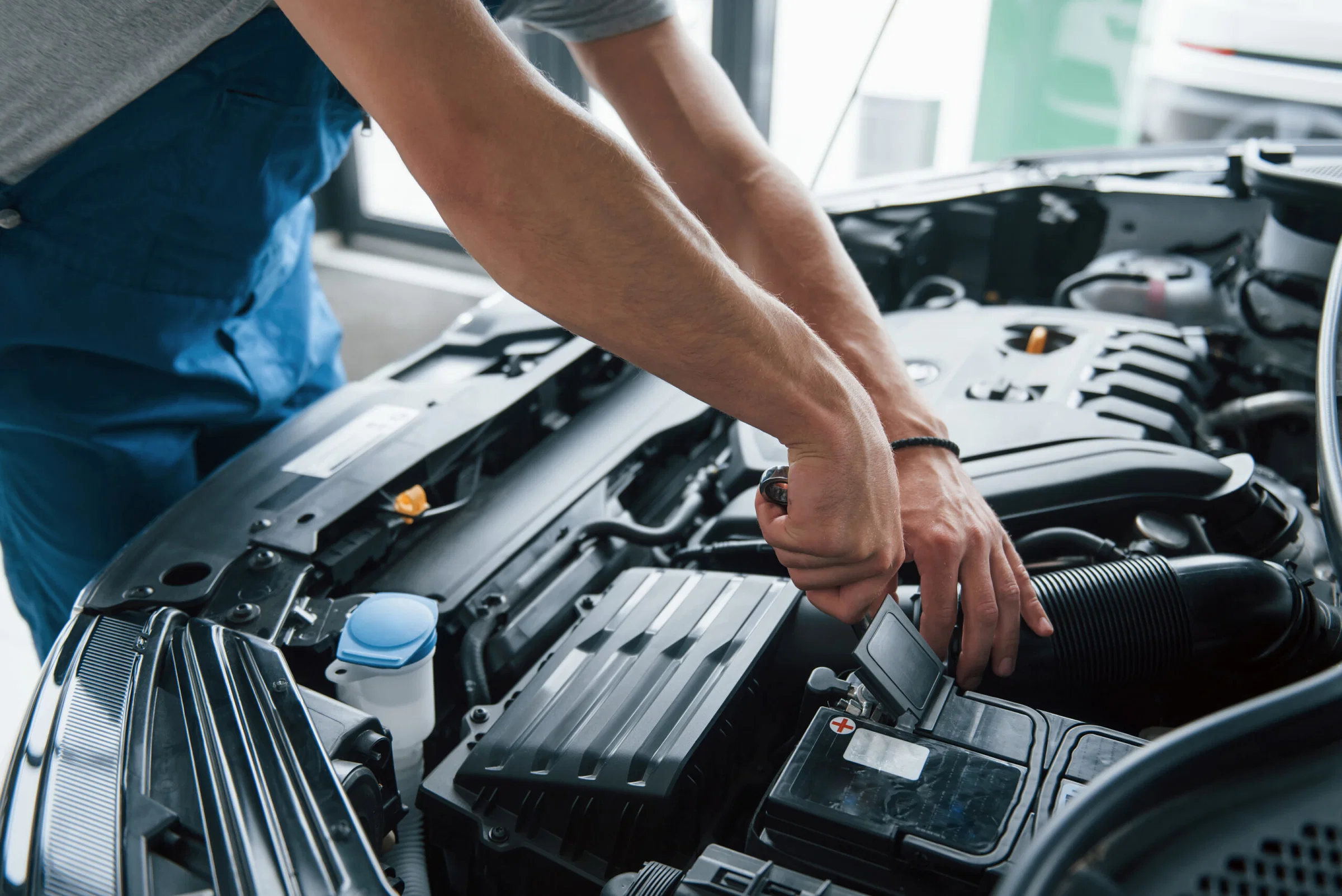 A person uses a wrench to work on the engine of a car with the hood open, performing maintenance or repair at a Santa Clara body shop. routine auto maintenance